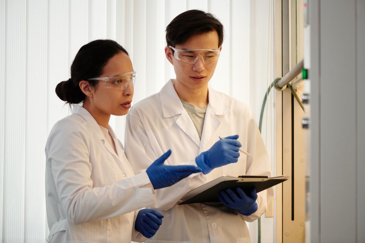group of scientists in white lab coats working with microscopes and digital devices